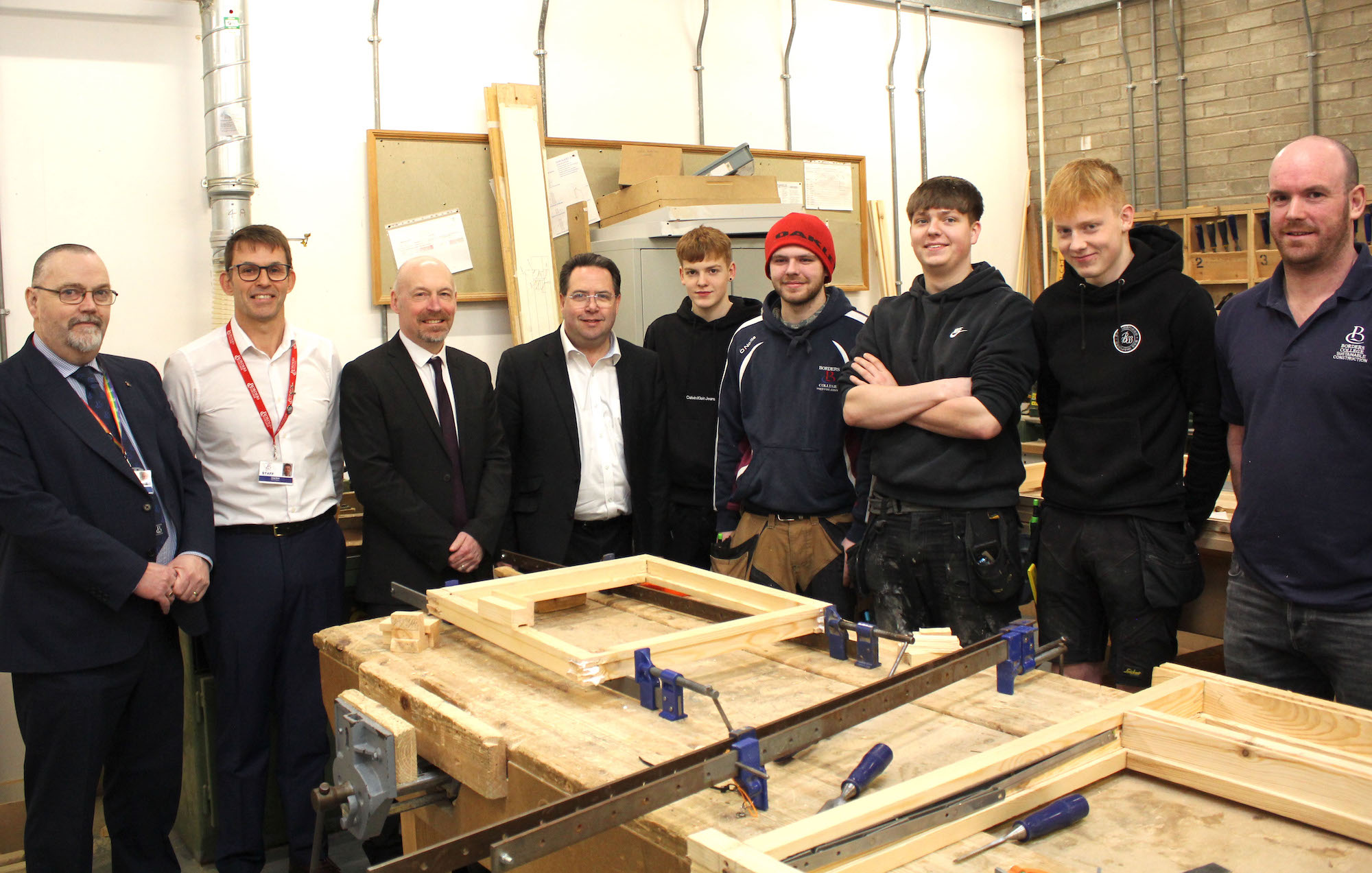 Group of staff and students, along with MSP Craig Hoy, standing in carpentry workshop